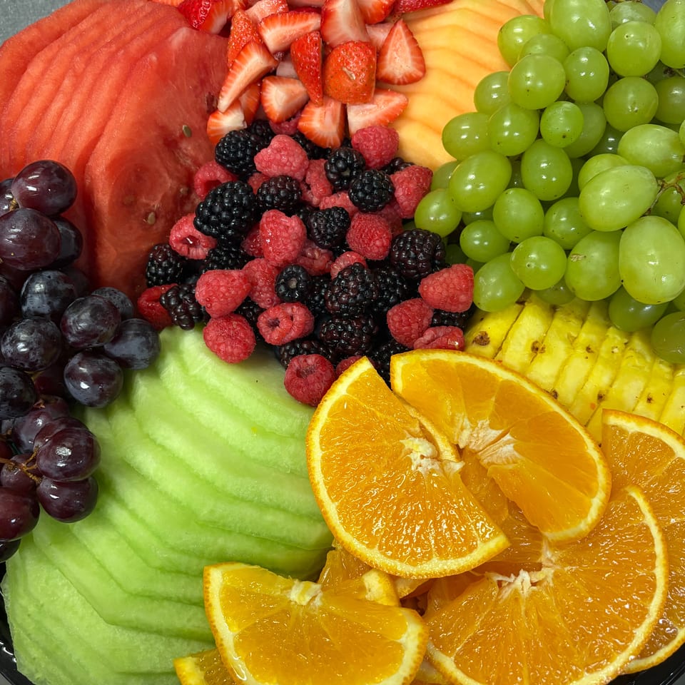 Colorful fruit platter featuring sliced watermelon, strawberries, cantaloupe, grapes, berries, honeydew, pineapple, and oranges.