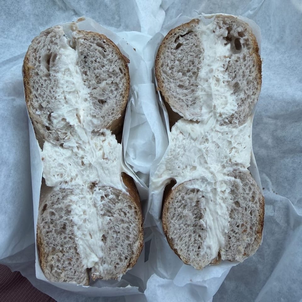 Four slices of rustic multigrain bread spread generously with creamy white cheese, arranged on parchment paper.