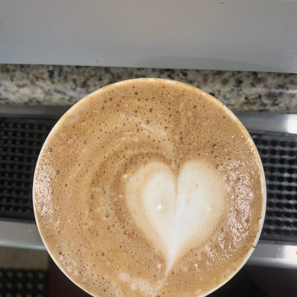 Top-down view of a foamy latte with white milk foam art in a cup on a speckled countertop.